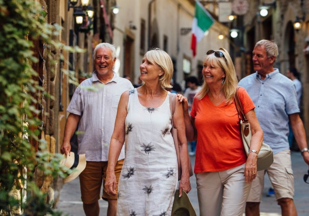 Mature couples looking around old town Italy as evening draws in. They walk down a narrow street while on holiday. Little lights can be seen outside of the buildings